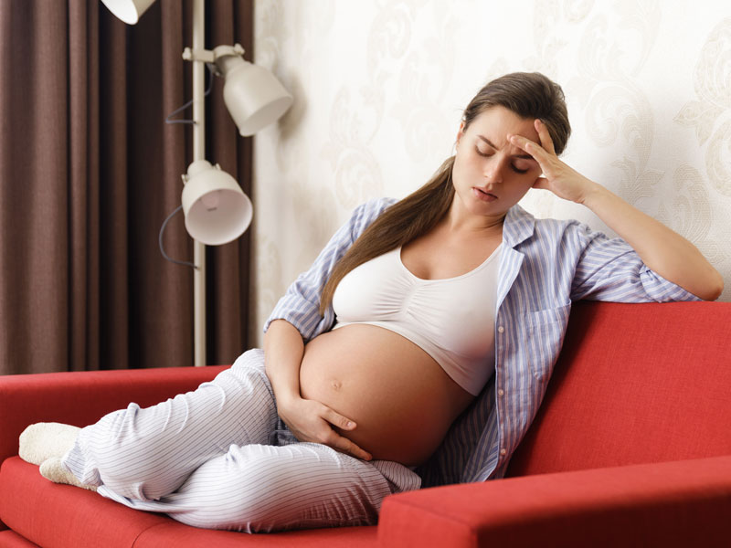 Young pregnant woman holding her head to illustrate common pregnancy concerns of fatigue