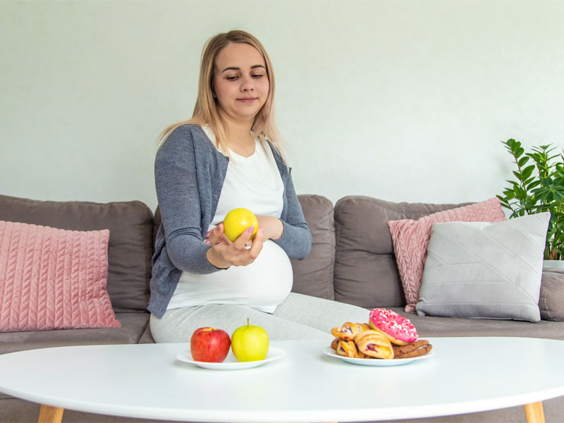 pregnant woman choosing an apple over sugary foods to illustrate gestational diabetes diet