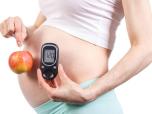 pregnant woman holding an apple and a blood sugar testing device to illustrate blood sugar control during gestational diabetes