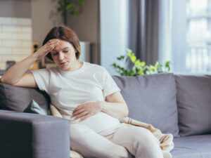 Pregnant woman on sofa at home looking tired to illustrate common symptoms of pregnancy