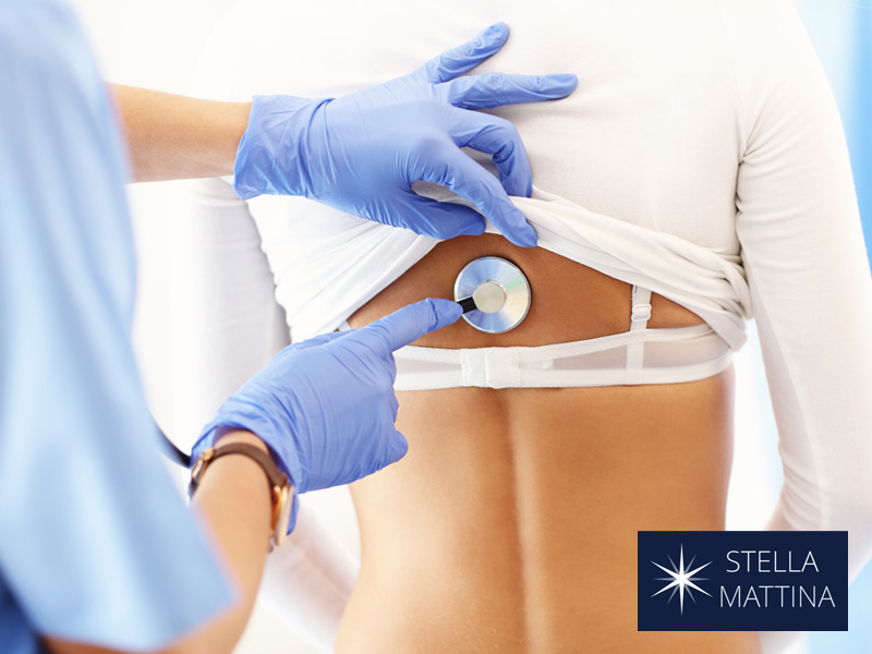 Doctor examining patient's back with stethoscope to illustrate annual exam for women