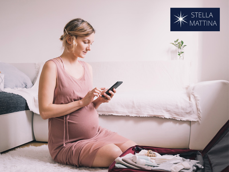 Heavily pregnant woman checking phone to illustrate consulting her third trimester checklist