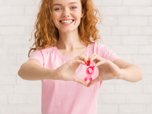 young woman making a heart shape around a breast cancer ribbon