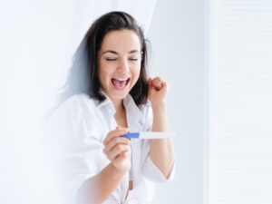 young woman viewing a positive pregnancy test to illustrate the importance of prenatal visits