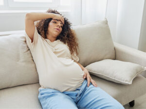 prenant woman on couch at home with severe headache to illustrate the need for treatment for preeclampsia