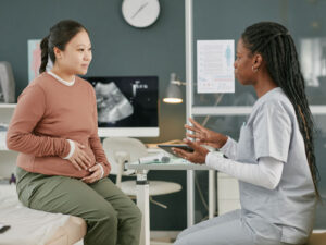 pregnant Asian adult talking with a docotr to illustrate the difference between an internal medicine doctor and a gynecologist