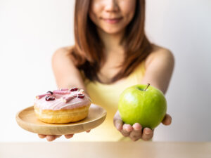 woman holding a cake and an apple to illustrate choosing healthy foods to help avoid hormonal imbalance
